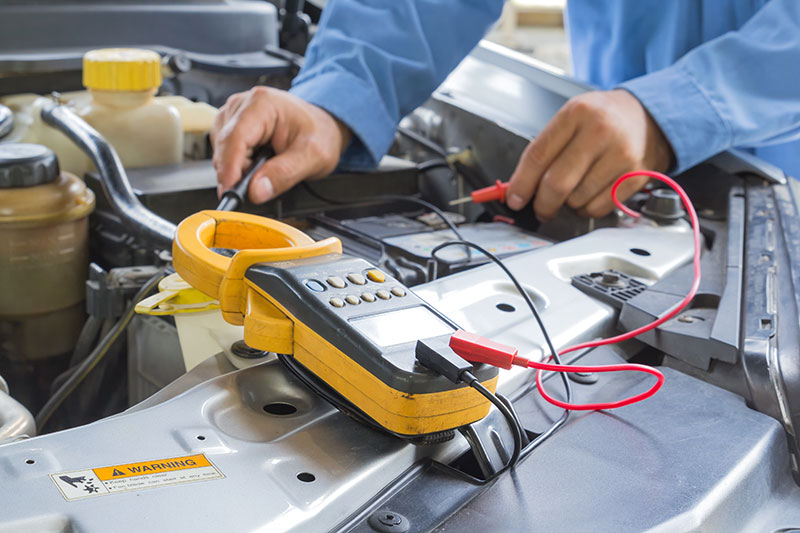 auto electrician checking battery with a multimeter