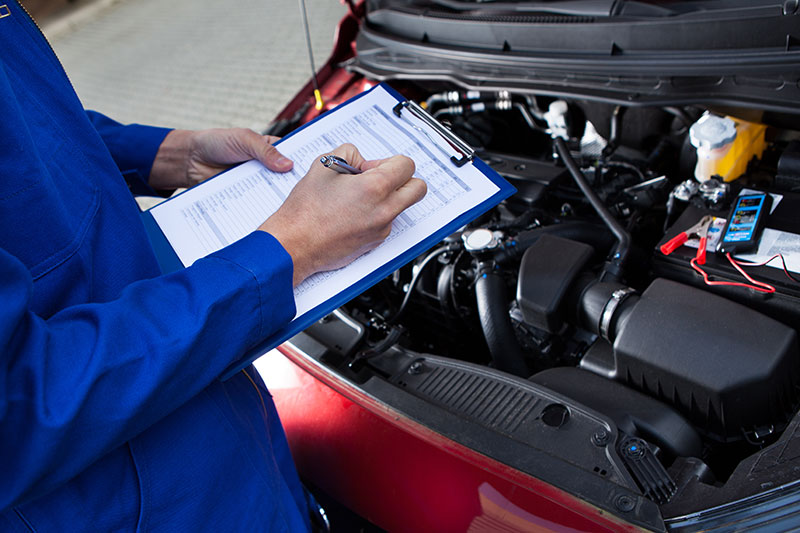 close up of mechanic inspecting vehicle with checklist